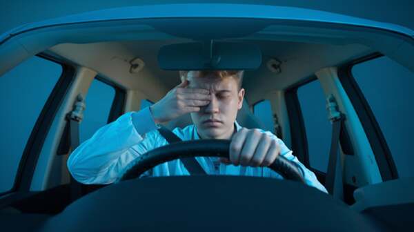 Tired driver rubbing eyes behind wheel showing sleep apnea driving safety risks